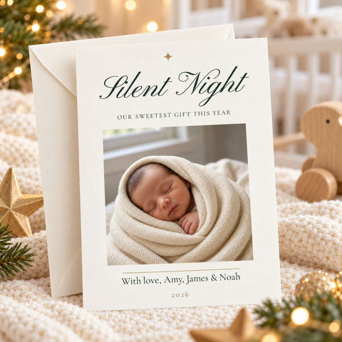 A personalized baby birth announcement card titled 'Silent Night' with a photo of a sleeping newborn swaddled in cream knit fabric, shown with an envelope on a cozy holiday-themed blanket with lights and wooden decor.